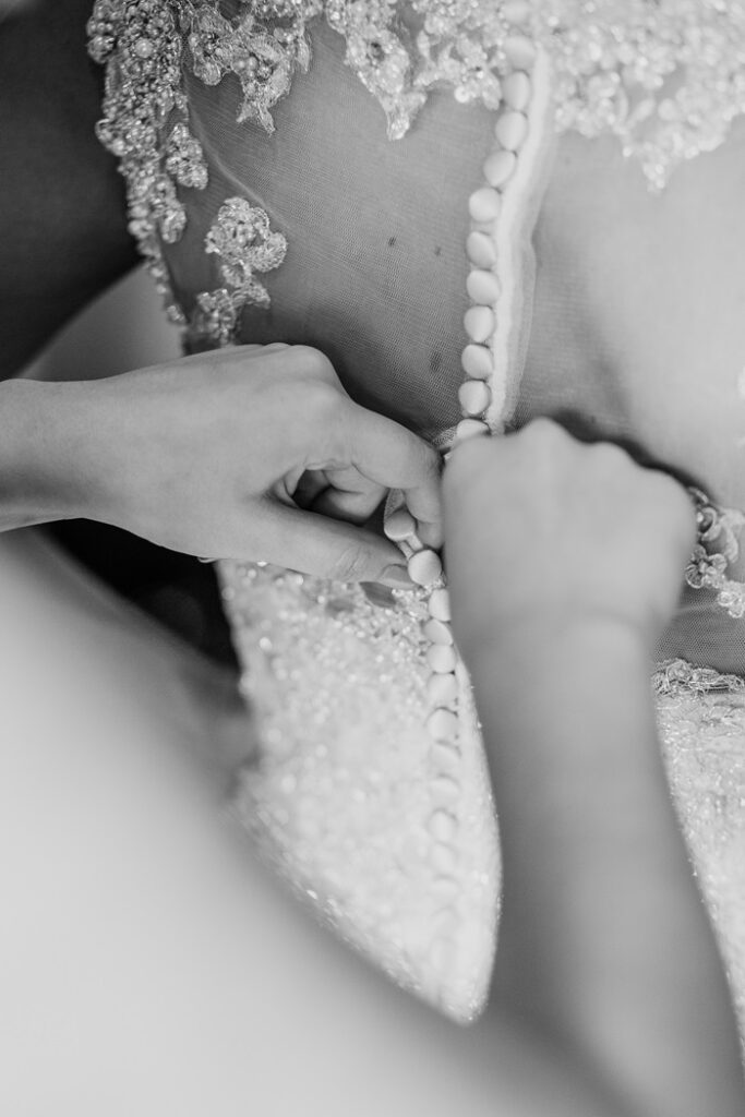 Bride getting dressed in her wedding dress before discussing bridal alterations costs with seamstress